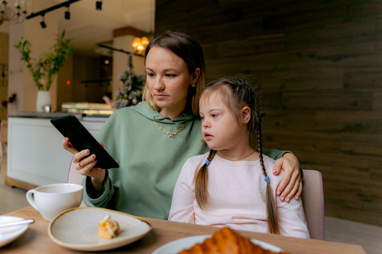 Mother and daughter bonding over a digital tablet in a cozy café setting.