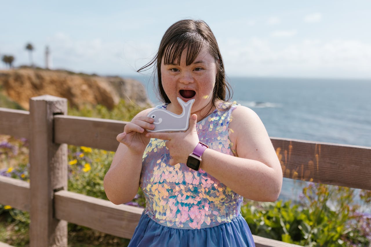 A joyful girl with Down Syndrome holding a whale toy by the sea.